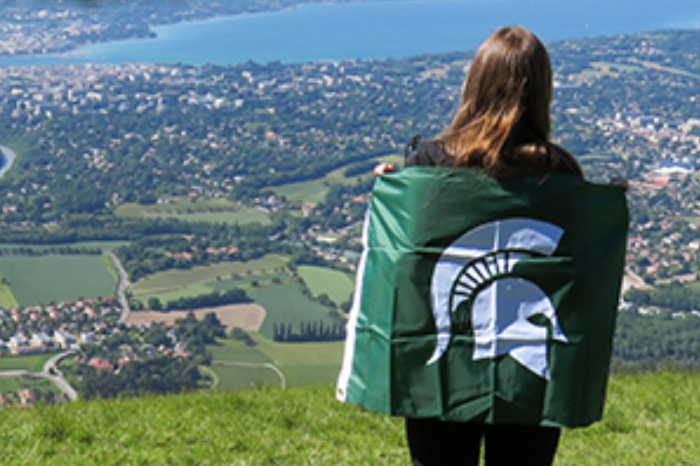MSU student on a study abroad trip posing with an Spartan flag.